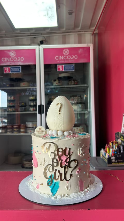 Gender reveal cake with cream frosting, question mark decoration, and boy or girl text on pink surface