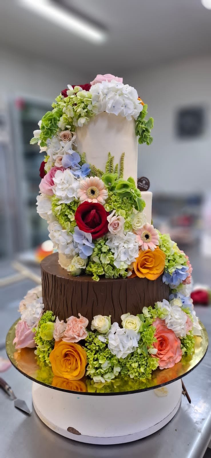 Three elegant engagement cakes on a gold tray, each decorated with ivory frosting, flowers, and topped with engagement ring toppers