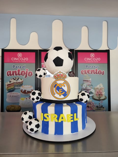 Real Madrid themed cake with soccer balls and blue and white striped base, decorated with club logo and topped with white fondant figures