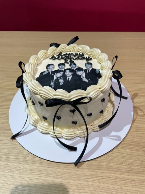 Decorated cake with cream frosting, black heart decorations, and a black and white photo of five men in suits on top, tied with black ribbons